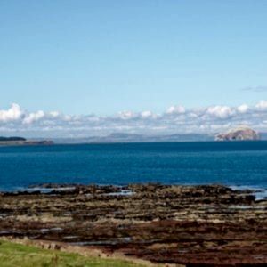 A view out over the Firth of Forth with a rocky shore in the foreground and a beautiful view across the water. The sky is blue and the clouds sit low in the sky.