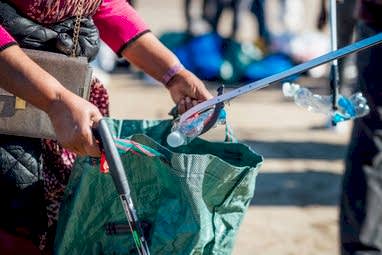 A close up of volunteers filling a bag with plastic bottles at a Scarborough beach clean.