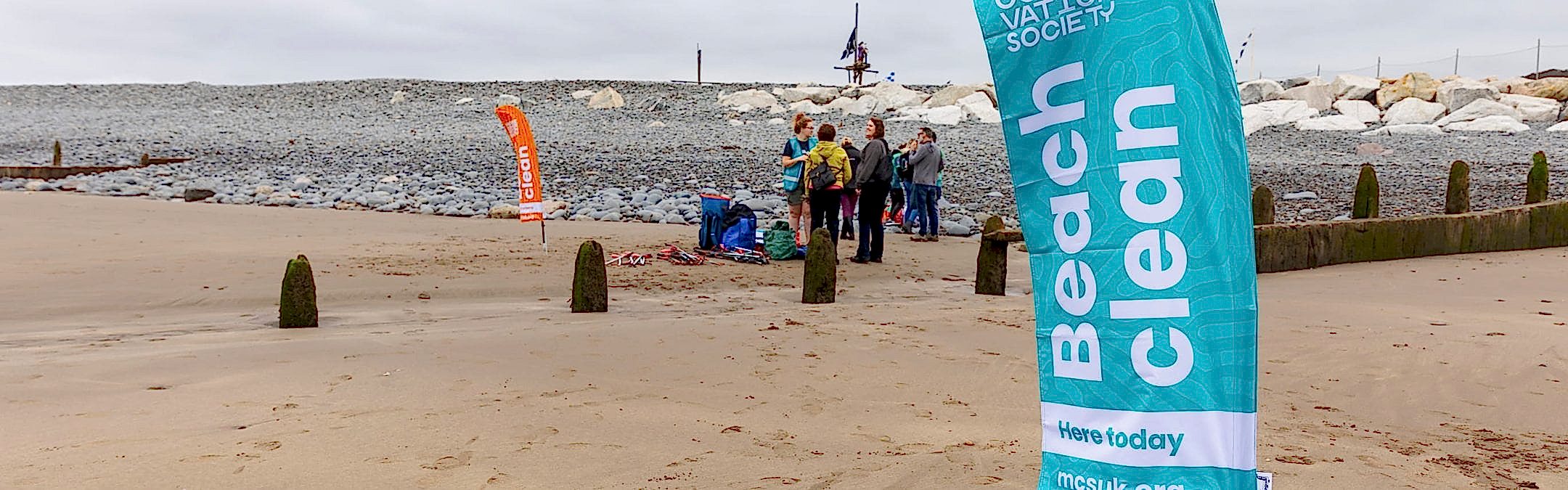 A beach with a flag in the foreground that reads "Marine Conservation Society Beach Clean"