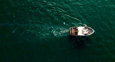 A small fishing trawler seen from a birds-eye-view over a deep blue ocean.