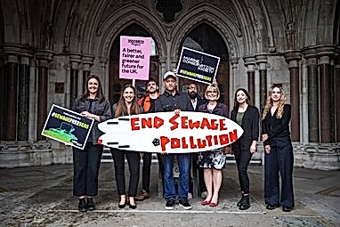 Members of the Marine Conservation Society team stand with other NGOs outside Westminster holding a surf board reading 'end sewage pollution'.