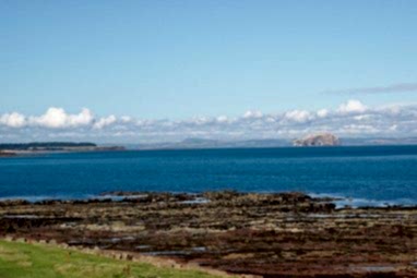 A view out over the Firth of Forth with a rocky shore in the foreground and a beautiful view across the water. The sky is blue and the clouds sit low in the sky.