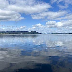 A photograph taken from the bank of the Dornoch Firth with far-reaching veiws across the calm water. The sky is blue with white clouds and across the water you can see the coastline where the Glenmorangie Distillery Company is based.