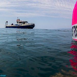 A fishing boat in shown in the distance with a bright pink buoy-type device reading 'ghost fishing UK' in the foreground.