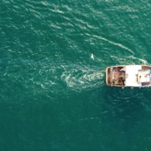 A small fishing trawler seen from a birds-eye-view over a deep blue ocean.